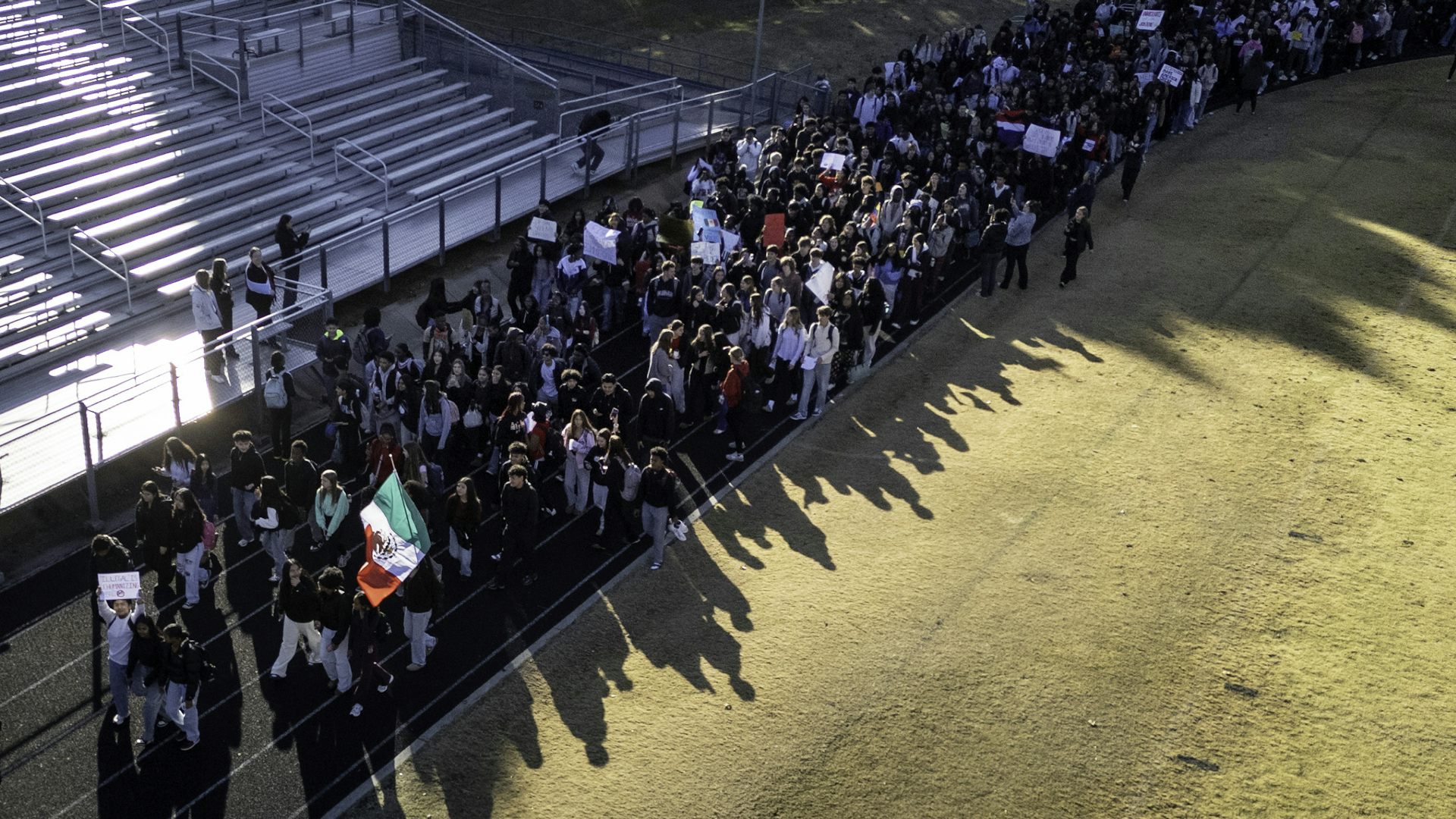 An aerial view shows a large group of people walking together on a track.