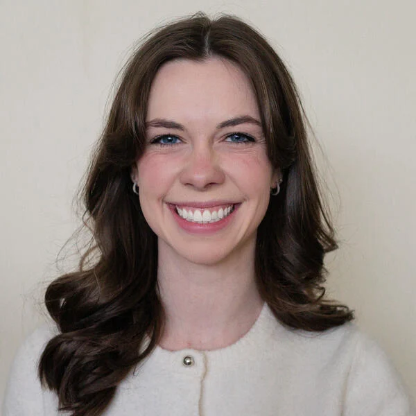 This photo depicts Ashley Mowreader smiling. She has long brown hair and is wearing a buttoned white shirt.