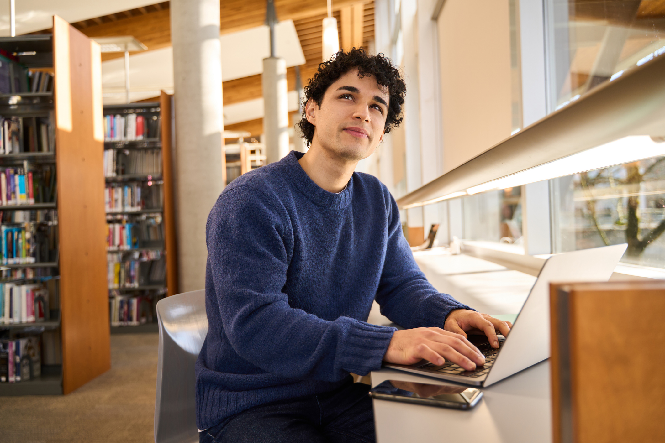 Pensive student thinking while working on laptop in library