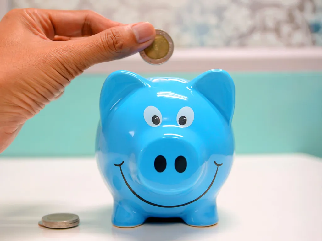 A hand inserting coins into a piggy bank