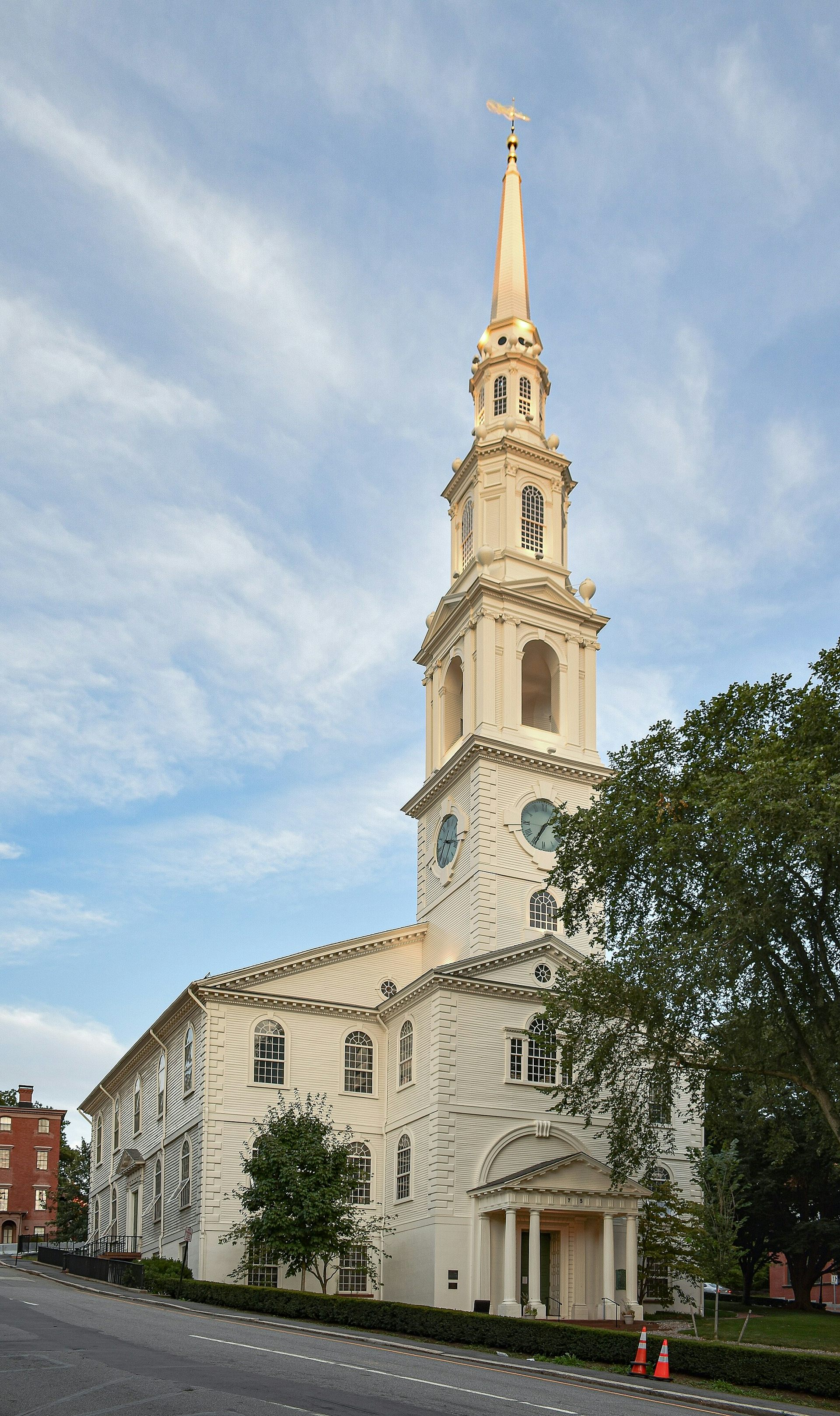 A white church with a tall steeple rising into a blue sky with wispy clouds.