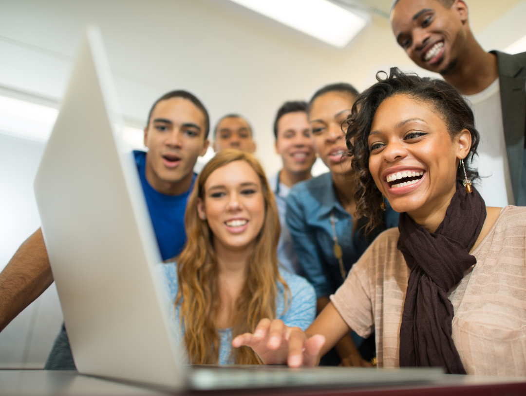 college student on laptop after getting accepted surrounded by friends
