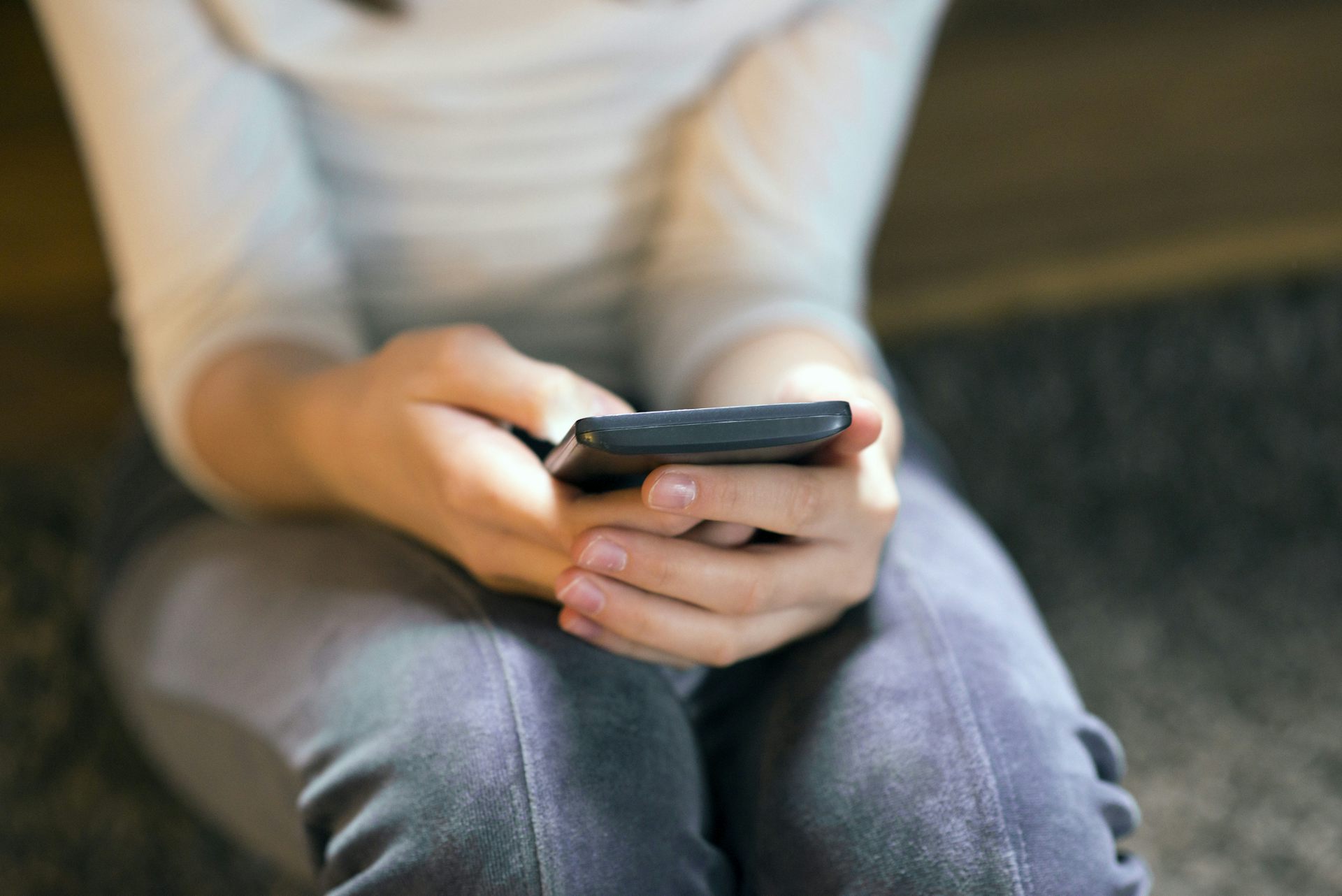 Person sitting against wall, arms on legs, typing on phone