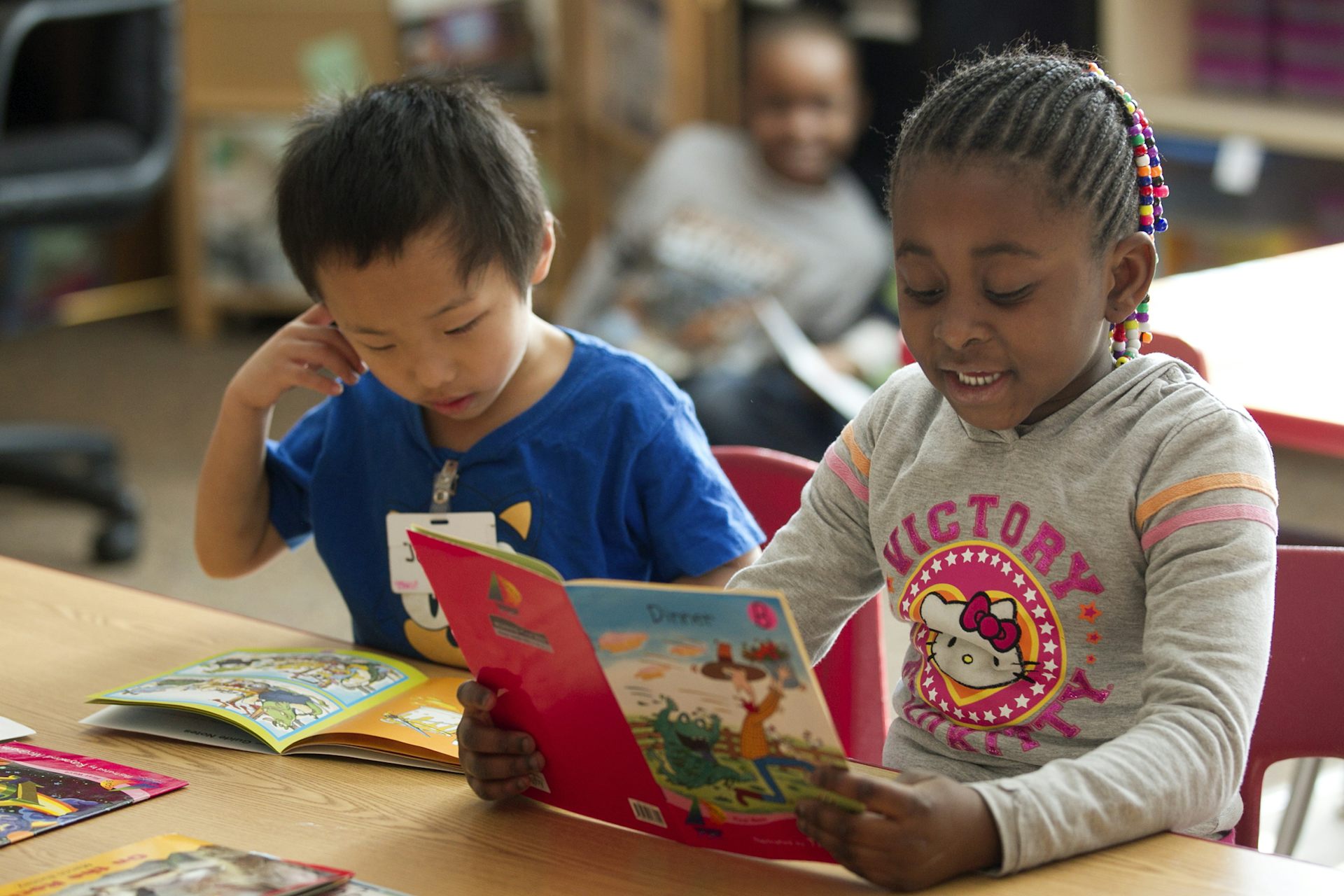 Two young children sit at a desk and read books.