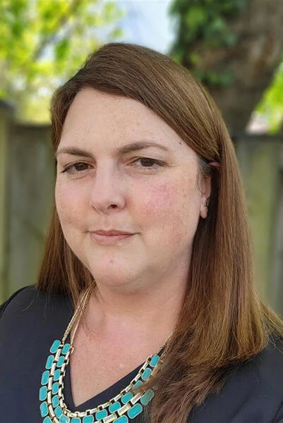 A portrait of Heather Parsons, a light-skinned woman with brown hair, wearing a blue top with a turquoise necklace.