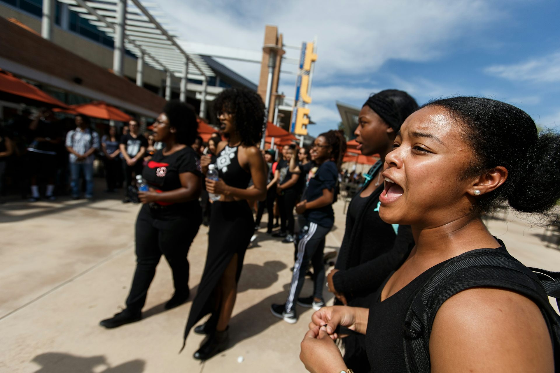A group of young Black women stand together and appear to be shouting.
