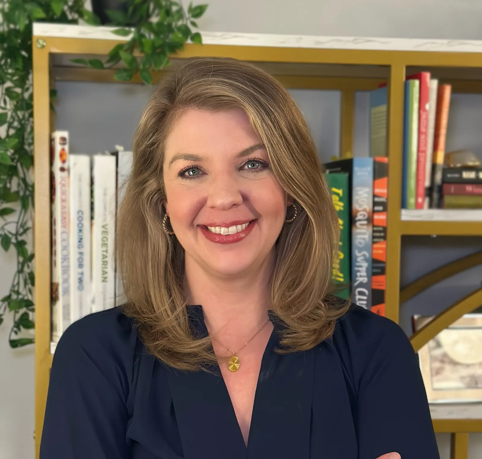 A headshot of a person. in the background is a bookcase