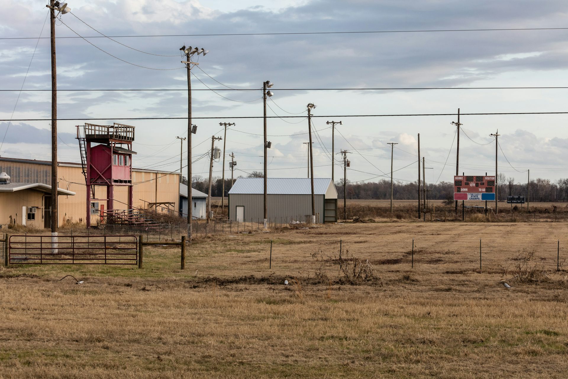 A scoreboard and old-looking building are seen in a brown field.