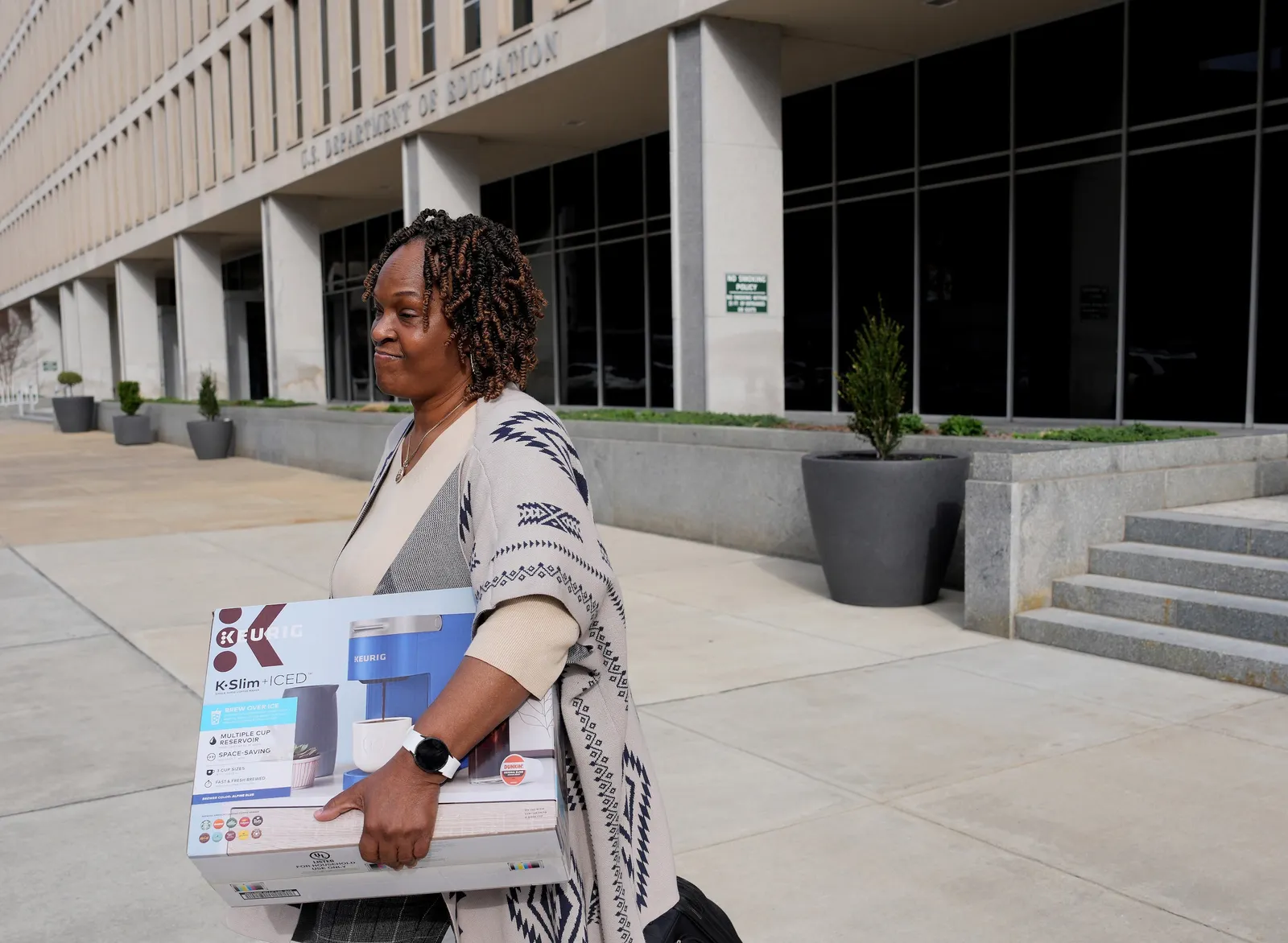 A person is walking outside teh Education Department in Washington, D.C. They are holding a box with belongings.