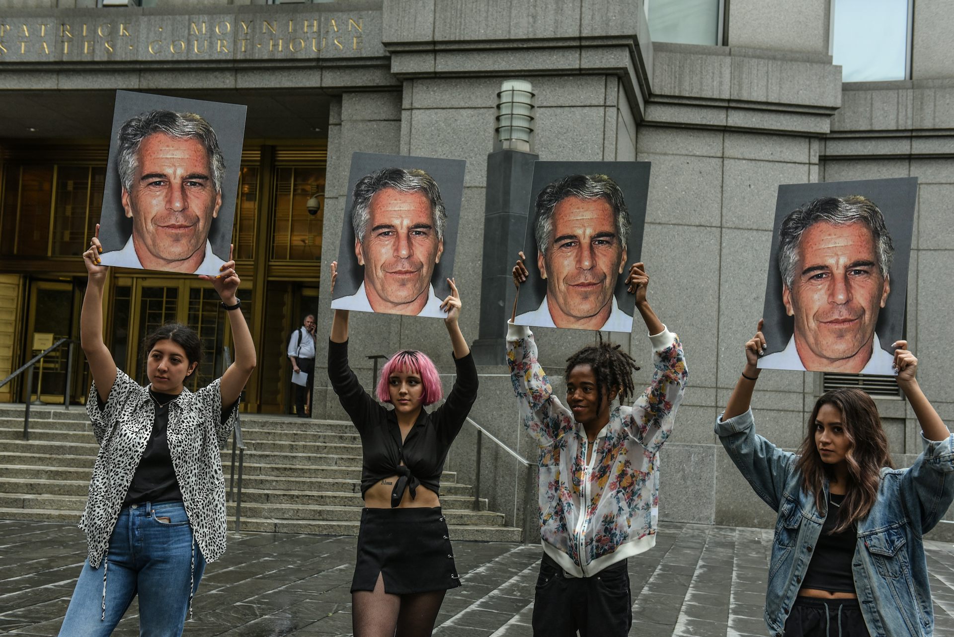 Four women hold photos of Jeffrey Epstein aloft.