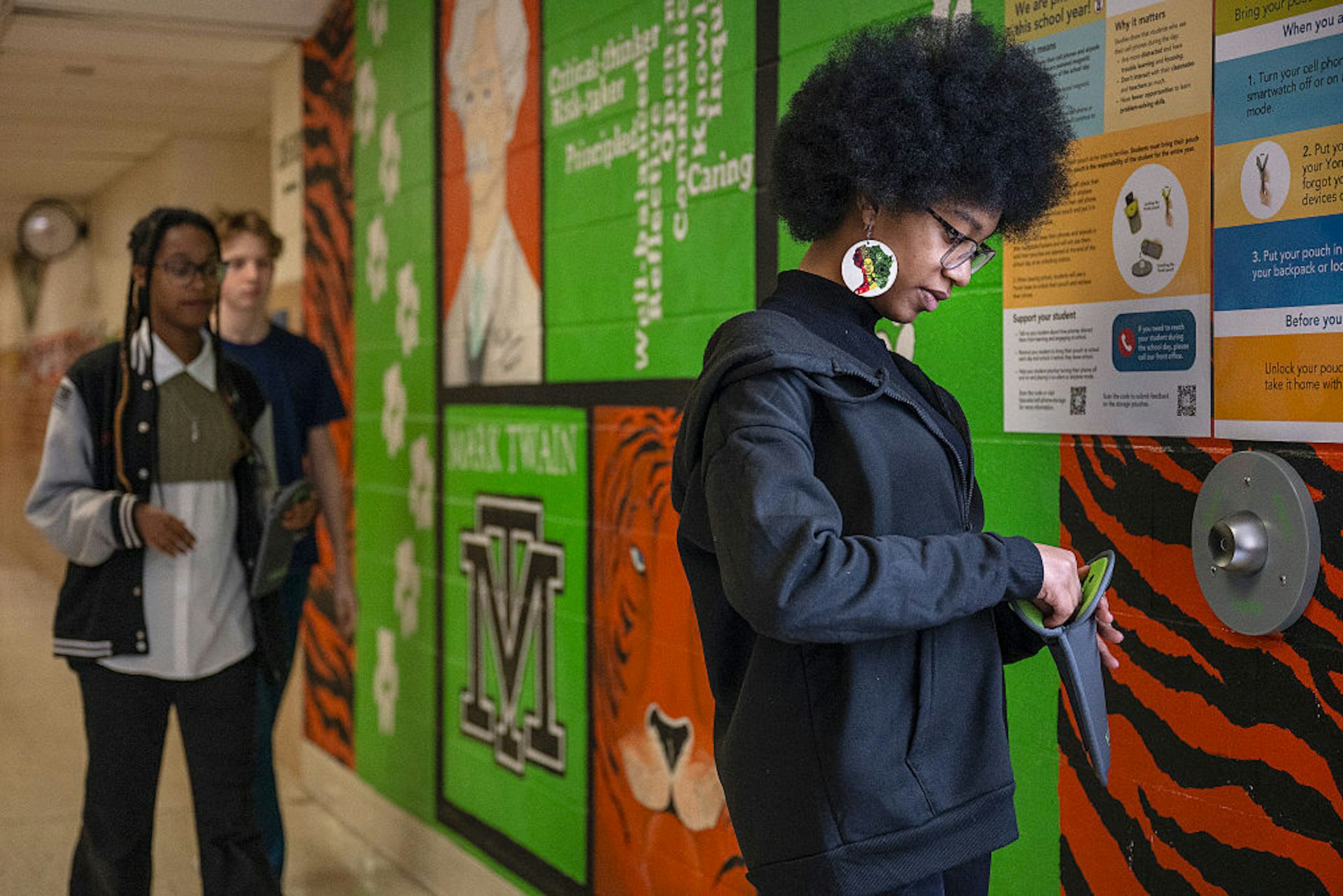 A young girl, as seen from the side, looks down at a dark pouch in a colorful hallway.