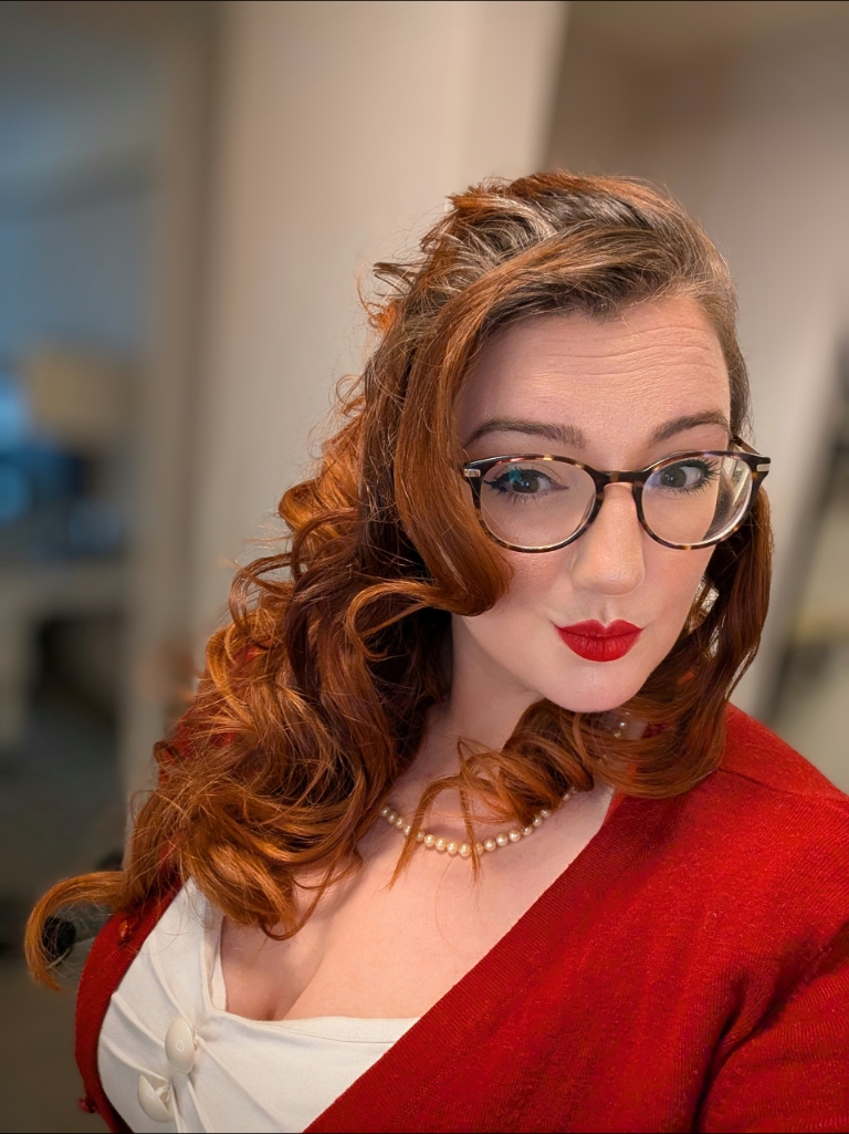 Dr. Vaughn Joy wears a red sweater, red lipstick, and cute glasses